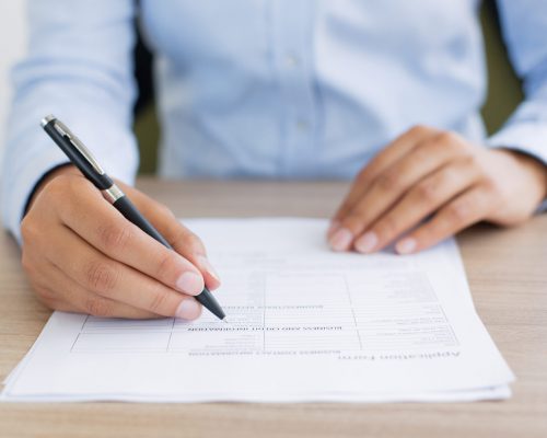 Cropped view of person holding pen and filling out application form on table